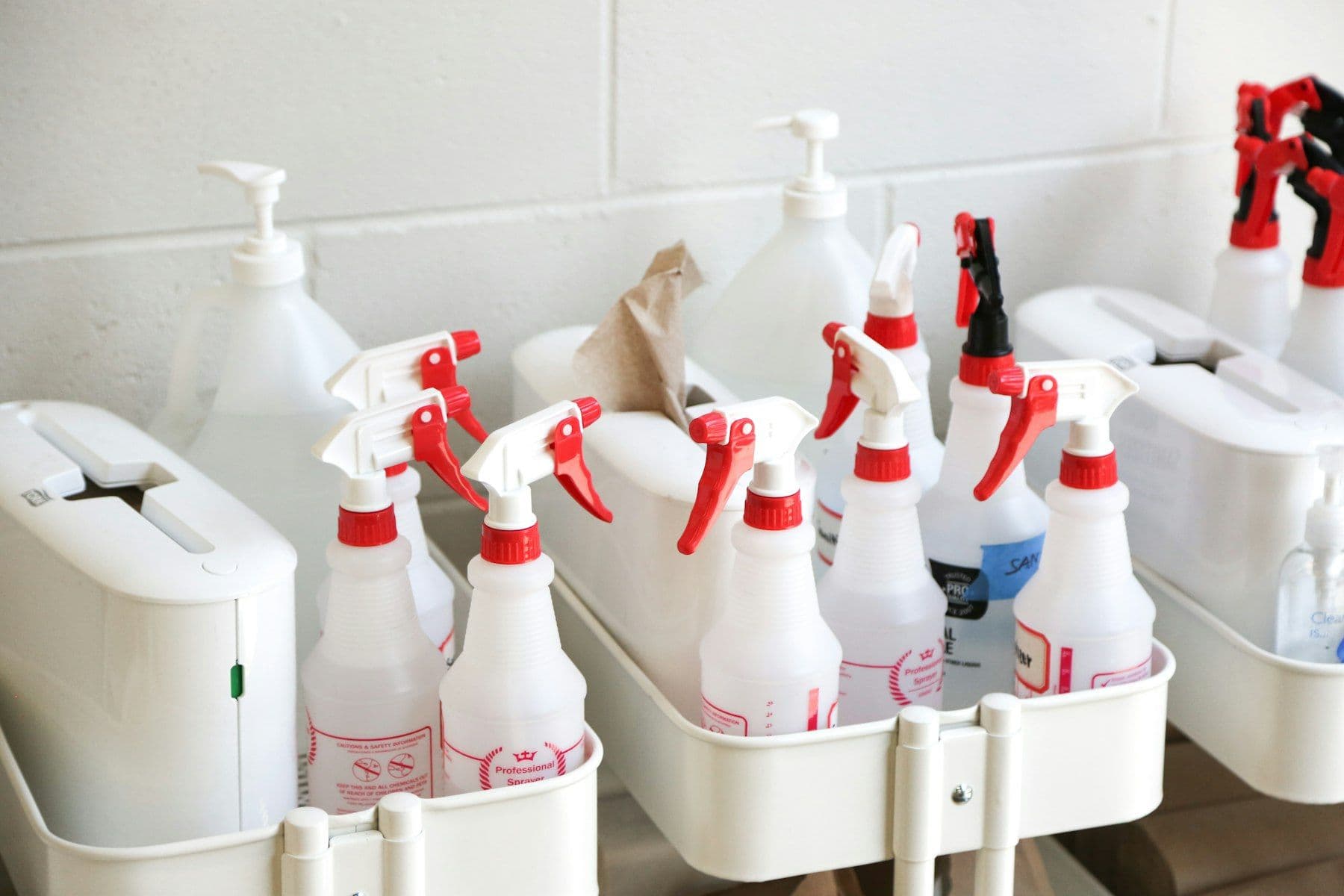 Rows of white trigger spray bottles in a cleaning caddy